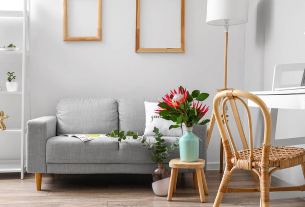 Mesa con flores de protea y sofá en el interior de la habitación - Foto, imagen