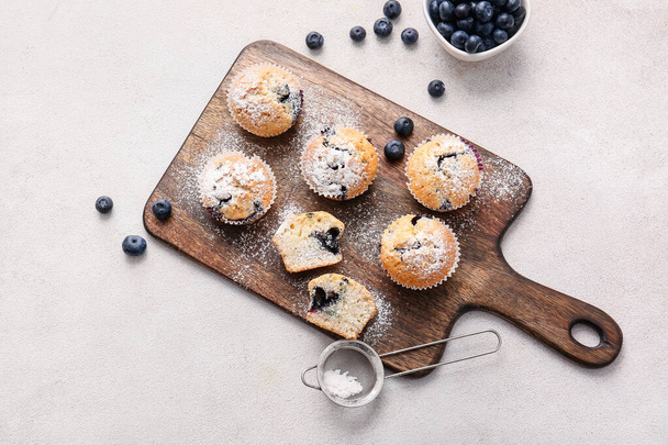 Board with tasty blueberry muffins on light background - Zdjęcie, obraz