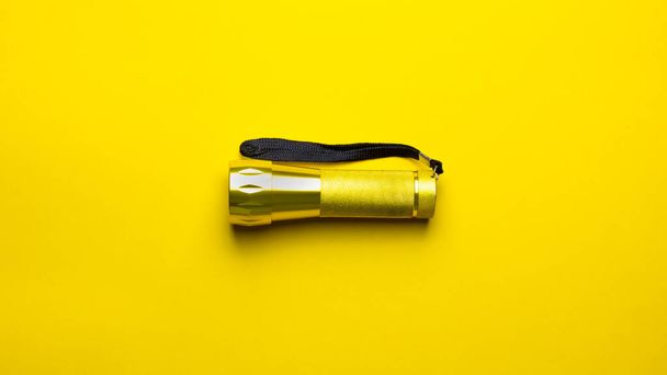 Gelbe Taschenlampe auf gelbem Hintergrund. Die Taschenlampe ist ausgeschaltet, hat einen Gurt, um sie an der Hand zu halten. - Foto, Bild