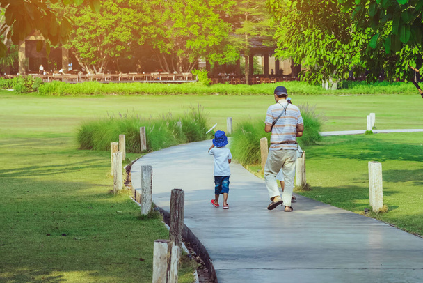 Visszapillantás ázsiai apa és fia séta útján zöld kertben.Apa és fia együtt sétálnak a parkban. Boldog család töltenek időt együtt kívül zöld természet. Családi idő fogalma. - Fotó, kép