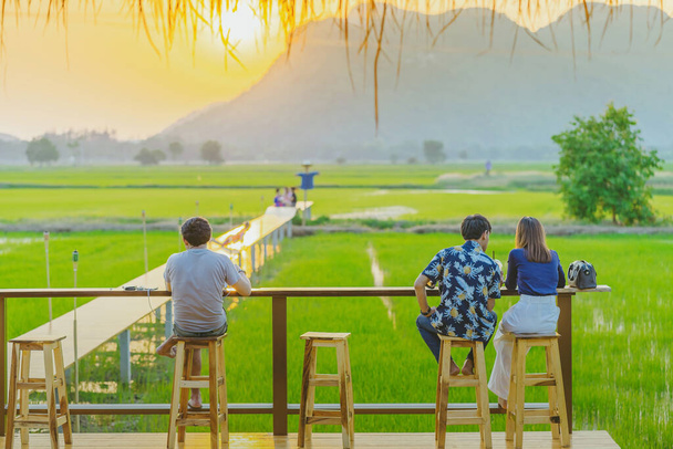 Vue arrière des gens assis pour se reposer et attendre le temps de prendre des photos du coucher du soleil sur le balcon de l'agriculteur dans les rizières. - Photo, image