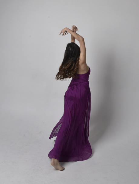 Full length  portrait of pretty brunette asian girl wearing purple flowing  gown. Standing, dancing pose on on studio background. - Фото, изображение