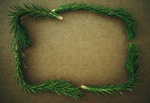 Noel ağaçlarının yeşil dalları, kahverengi arka planda dikdörtgen bir çerçeve içinde katlanmış, bir tebrik metni için bir yer. - Fotoğraf, Görsel