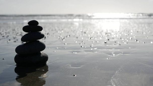 Камень балансирует на берегу океана, камни укладываются морскими волнами. Пирамида гальки на песчаном берегу - Фото, изображение