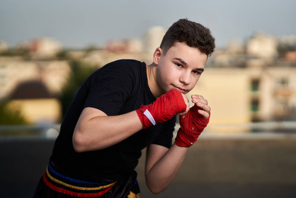 Young teenage kickboxer fighter training on the roof with buildings in background, urban warrior - Zdjęcie, obraz