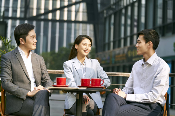 three asian corporate businesspeople discussing business outdoors in coffee shot - Photo, Image