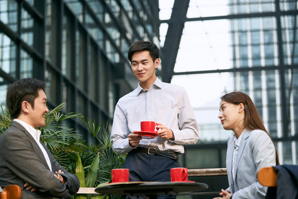 drie aziatische zakenmensen praten chatten in een outdoor coffeeshop gelukkig en glimlachend - Foto, afbeelding