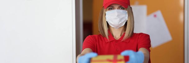 Woman courier in protective medical mask and gloves giving gift - 写真・画像