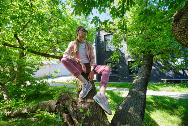 Young woman sits on crooked tree trunk in sunny day - Foto, afbeelding