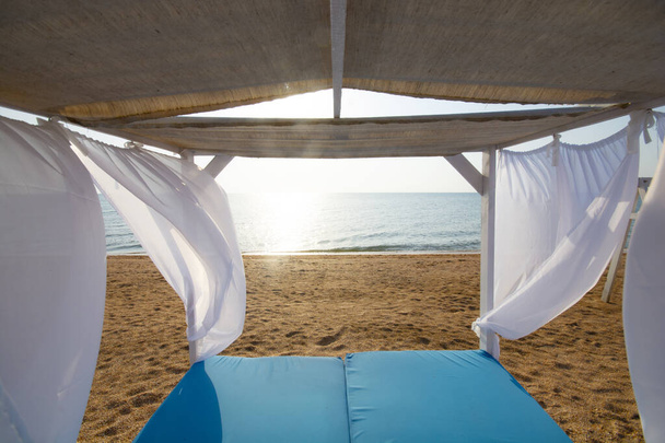 Morning beach scene through the blue canopy with white curtains for luxury summer relaxation. - Foto, Imagen