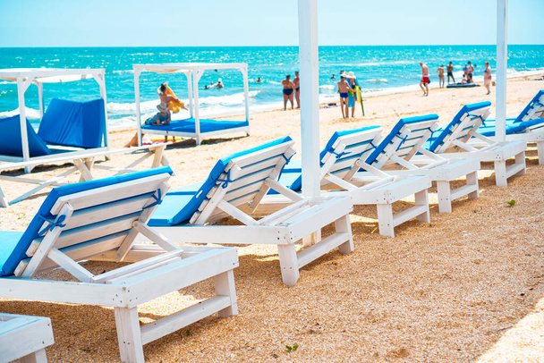 Sun loungers on the beach near the blue sea. People on the beach is not recognizable. - Foto, Imagen