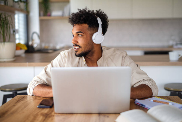 Young man student with laptop and headphones indoors at home, studying. - Foto, Imagen