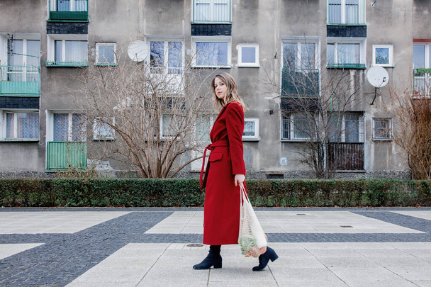 Donna di stile in cappotto rosso e borsa a rete svegliarsi a casa dopo lo shopping. Paesi dell'Europa orientale
  - Foto, immagini