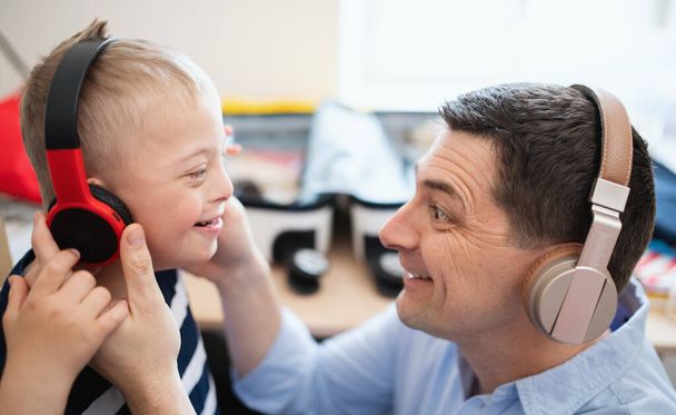 Father with happy down syndrome son indoors at home, using headphones. - Fotoğraf, Görsel