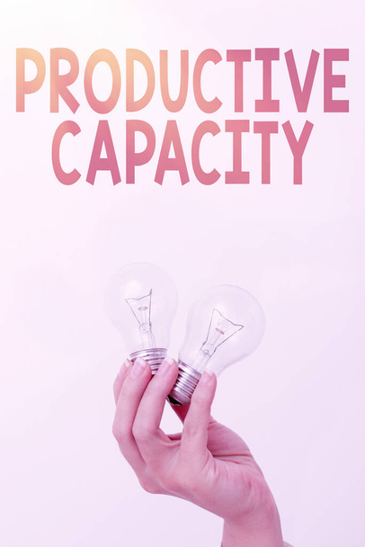 Text sign showing Productive Capacity. Business overview the maximum possible output of a production plant Hand holding two lamp showing or presenting new technology ideas - Zdjęcie, obraz