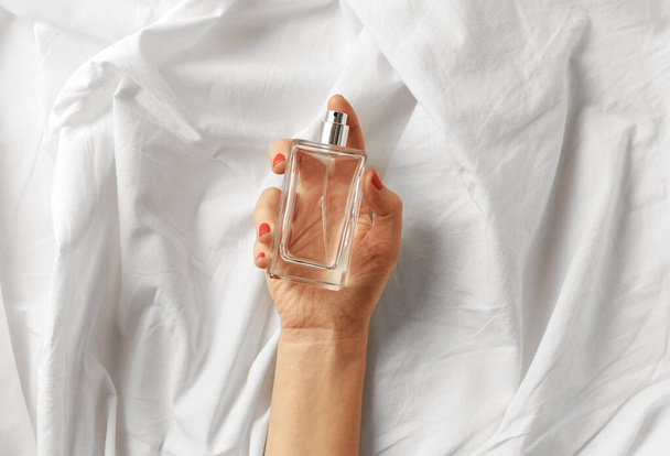 female hand with bottle of perfume on white sheet - Foto, Imagen