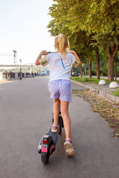 Een meisje van 8 jaar oud rijdt op een gehuurde elektrische scooter in het park. Schopscooter delen - Foto, afbeelding