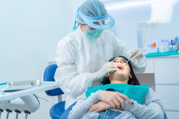 アジアの女性のアシスタントヘルパーヘルプ、治療のための歯科外科的光を調整することで医師をサポートします。専門歯科診療所の椅子に横たわっ若い女の子の患者の歯をチェックまたは検査 - 写真・画像