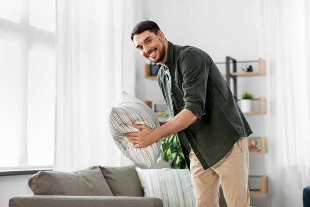happy smiling man arranging sofa cushions at home - Photo, image