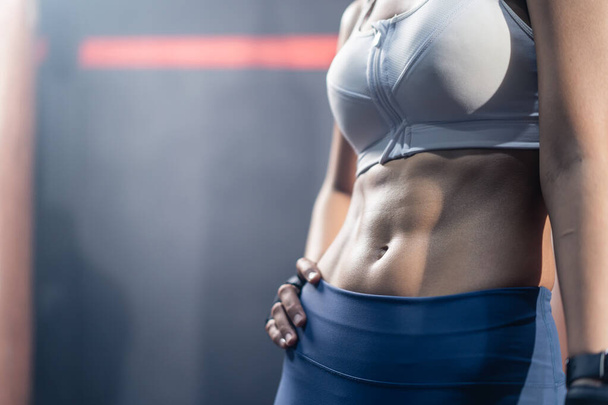 Close up of Athlete fit and firm girl stand with confidence after abdomen cardio workout exercise in stadium. Active sportswoman fitness trainer in sportswear show six pack and abs muscle at gym club. - Photo, Image