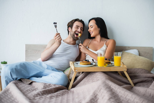 smiling woman feeding boyfriend with tasty pancakes in bed - Photo, Image