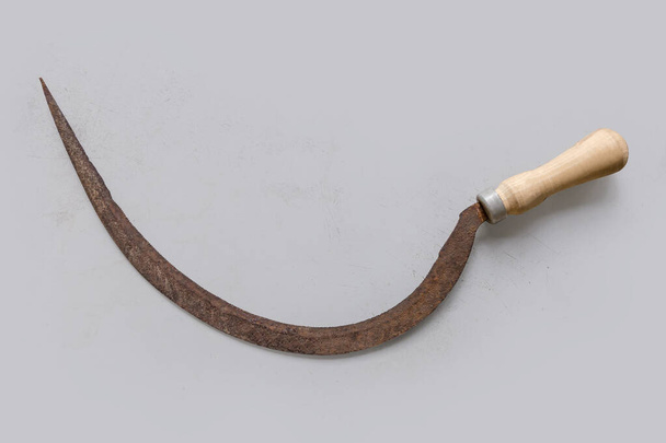 Старый ржавый серп с мелко зазубренным полукруглым лезвием и деревянной ручкой на легкой поверхности, вид сверху - Фото, изображение