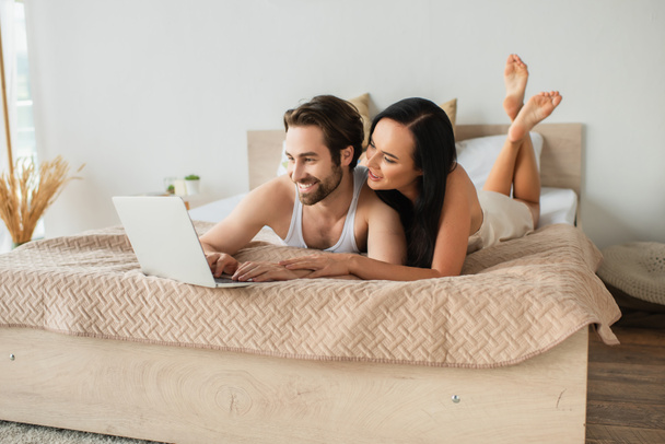 happy couple watching movie on laptop while lying on bed  - Foto, imagen