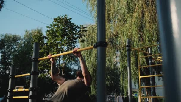 Homme caucasien se tire vers le haut sur la barre horizontale par le bas avec deux mains. Activités sportives en plein air et mode de vie sain. Exercices de fitness et de force pour les bras. Se réchauffer avant l'entraînement. - Séquence, vidéo