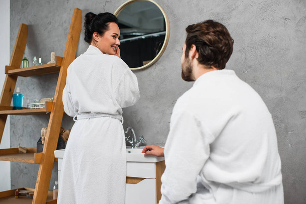 счастливая женщина в халате смотрит на парня в ванной  - Фото, изображение