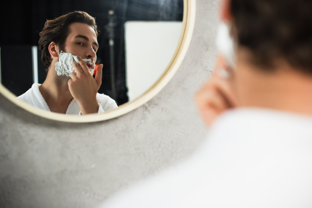 man applying shaving foam on face near mirror - Φωτογραφία, εικόνα