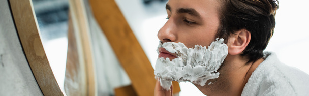 man applying shaving cream on face near mirror, banner - Фото, зображення