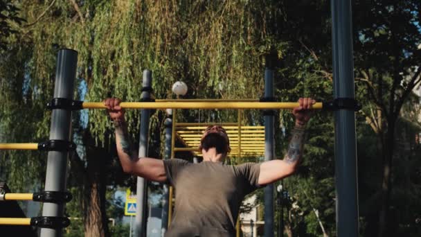 Blanke man trekt zich omhoog op horizontale balk van onderen met twee handen. Sportactiviteiten op het terrein en een gezonde levensstijl. Fitness en krachttraining voor armen. Opwarmen voor de training. - Video