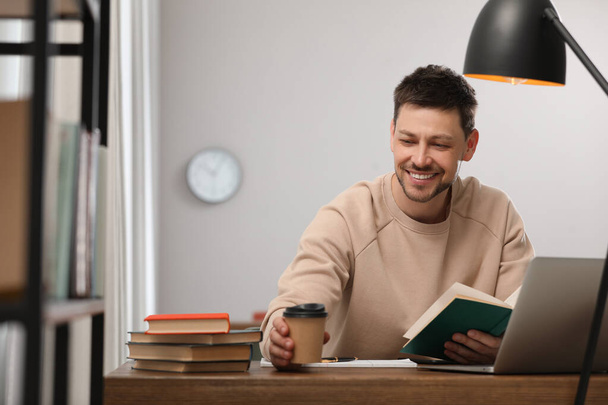 Happy man with cup of coffee studying in library - Foto, Bild