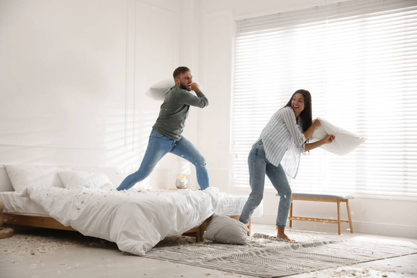 Happy young couple having fun pillow fight in bedroom - 写真・画像