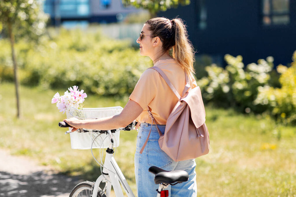 женщина с цветами в велосипедной корзине в городе - Фото, изображение