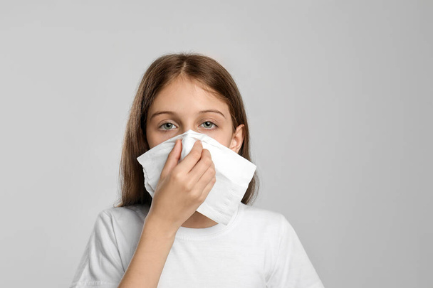 Little girl blowing nose into paper tissue on light grey background. Seasonal allergy - Foto, Bild