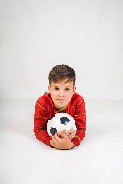 portrait of a happy young football player in a red uniform lying with a soccer ball on a white background with a place for text - Φωτογραφία, εικόνα