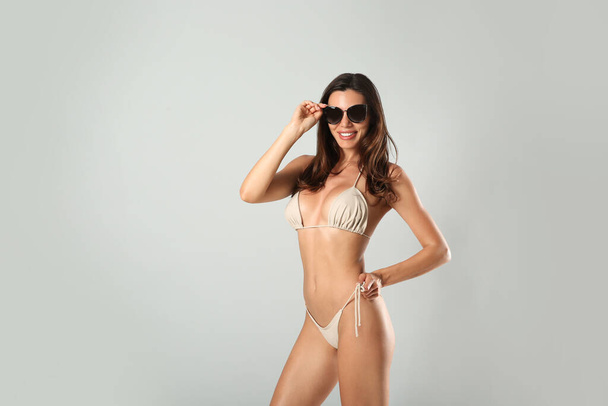 Beautiful woman in stylish bikini and sunglasses on light grey background. Space for text - Valokuva, kuva