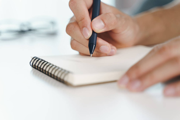 Κοντινό πλάνο του νεαρού άνδρα σε casual χέρια ύφασμα γράφοντας κάτω στο σημειωματάριο, σημειωματάριο χρησιμοποιώντας στυλό διαρκείας στο τραπέζι. - Φωτογραφία, εικόνα