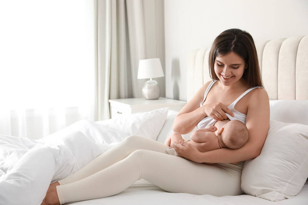 Young woman breastfeeding her little baby on bed at home - Fotó, kép
