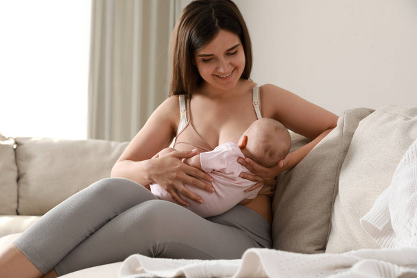 Jonge vrouw borstvoeding haar kleine baby op de bank thuis - Foto, afbeelding