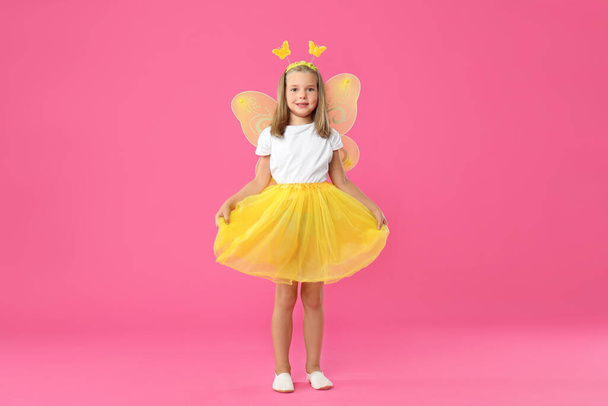 Cute little girl in fairy costume with yellow wings on pink background - Fotografie, Obrázek