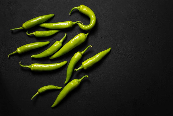 hromadu horkých zelených chilli papriček na černém povrchu. Pohled shora, kopie místa, vodorovně - Fotografie, Obrázek