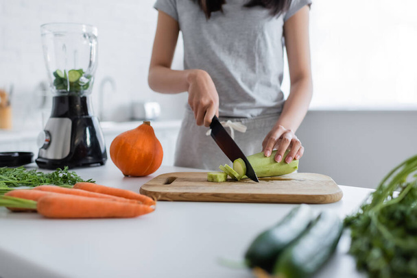 cropped view of woman cutting fresh zucchini near electric shaker and vegetables - Foto, Imagem