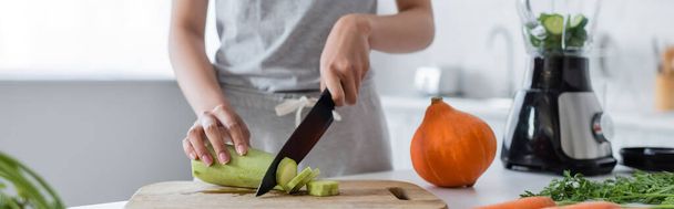 partial view of woman cutting zucchini near ripe pumpkin and blender with sliced cucumber, banner - Fotó, kép