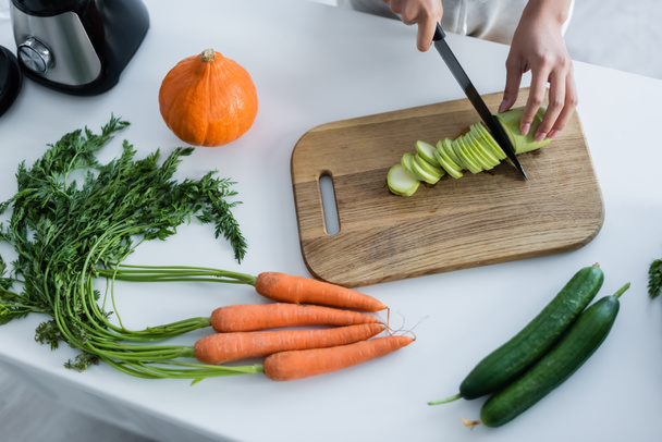 partial view of woman cutting zucchini on chopping board near fresh vegetables in kitchen - Foto, Bild