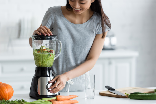 happy asian woman preparing vegetable smoothie for breakfast in kitchen - Фото, изображение