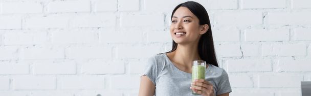 young asian woman with glass of fresh smoothie smiling while looking away, banner - Φωτογραφία, εικόνα
