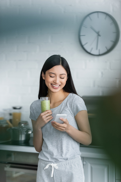 glückliche asiatische Frau mit Handy, während sie ein Glas leckeren Smoothie in der Hand hält - Foto, Bild