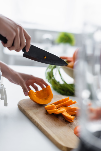partial view of woman with knife near ripe pumpkin on cutting board, blurred foreground - Foto, afbeelding